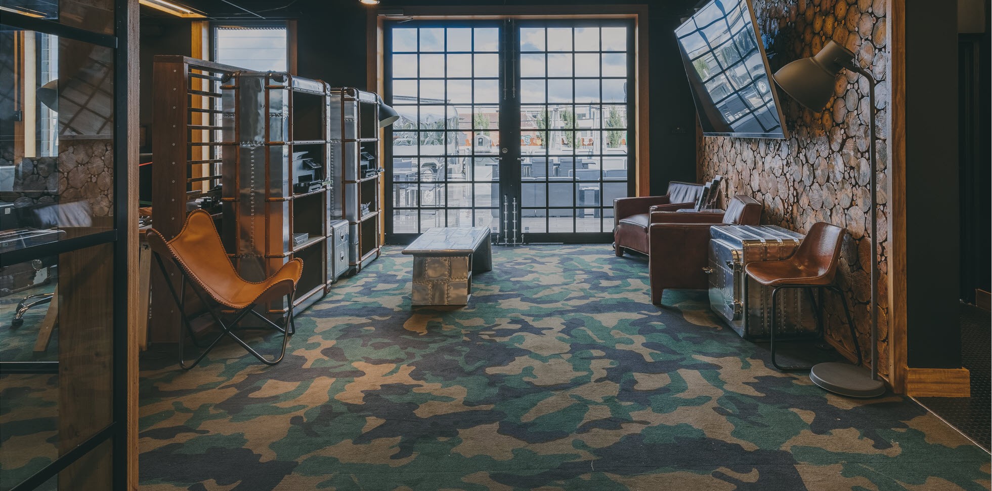 Stylish room at Deskplex Office Space Hawthorn Richmond Abbotsford with industrial decor, large windows, and a mix of leather seating, metal shelving, and a wood-patterned wall