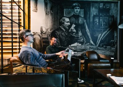 Modern lounge area at Deskplex Office Space Hawthorn Richmond Abbotsford, featuring a monochromatic mural, leather chairs, a wooden table, and an industrial-style lamp, creating a stylish blend of work and relaxation space