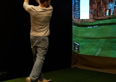 Person using a golf simulator at Deskplex Office Space Hawthorn Richmond Abbotsford, engaged in mid-swing. The screen displays a virtual golf course with data metrics such as speed, distance, launch angle, spin rate, and ball speed