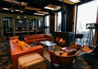 Modern coworking lounge with leather sofas, fireplace, and open office workspaces, featuring a professional remote work environment with industrial interior design.