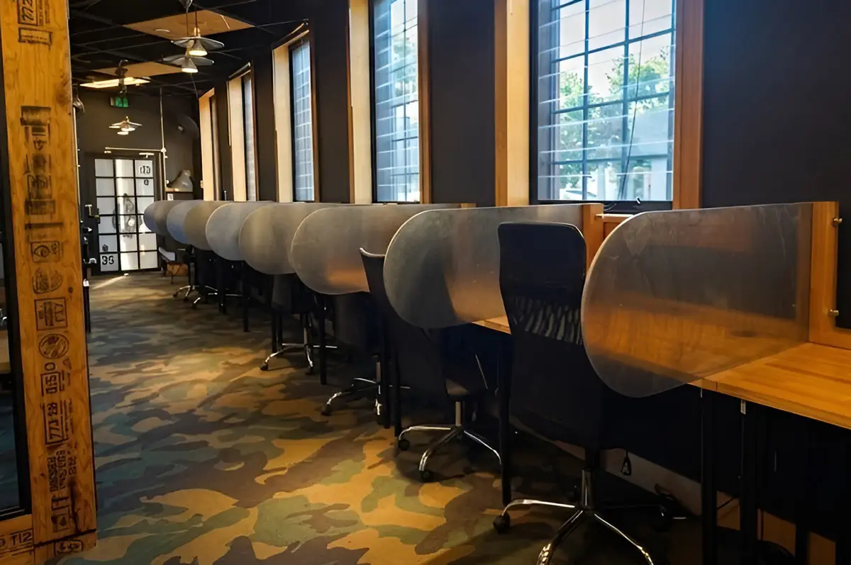 Three people at Deskplex Office Space Hawthorn Richmond Abbotsford are engaged in a collaborative discussion around a wooden table with laptops, a smartphone, and a piece of paper with images. The room has modern design elements with dark walls and wooden accents
