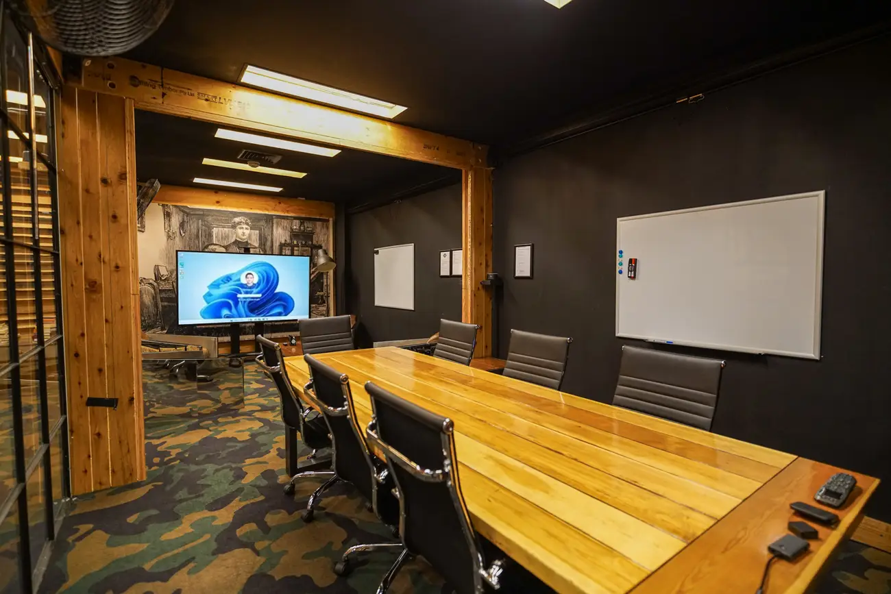 Stylish corporate boardroom featuring a large wooden conference table, ergonomic office chairs, interactive display screen, and modern industrial office design.