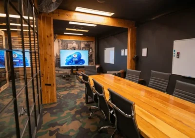 Stylish corporate boardroom featuring a large wooden conference table, ergonomic office chairs, interactive display screen, and modern industrial office design.