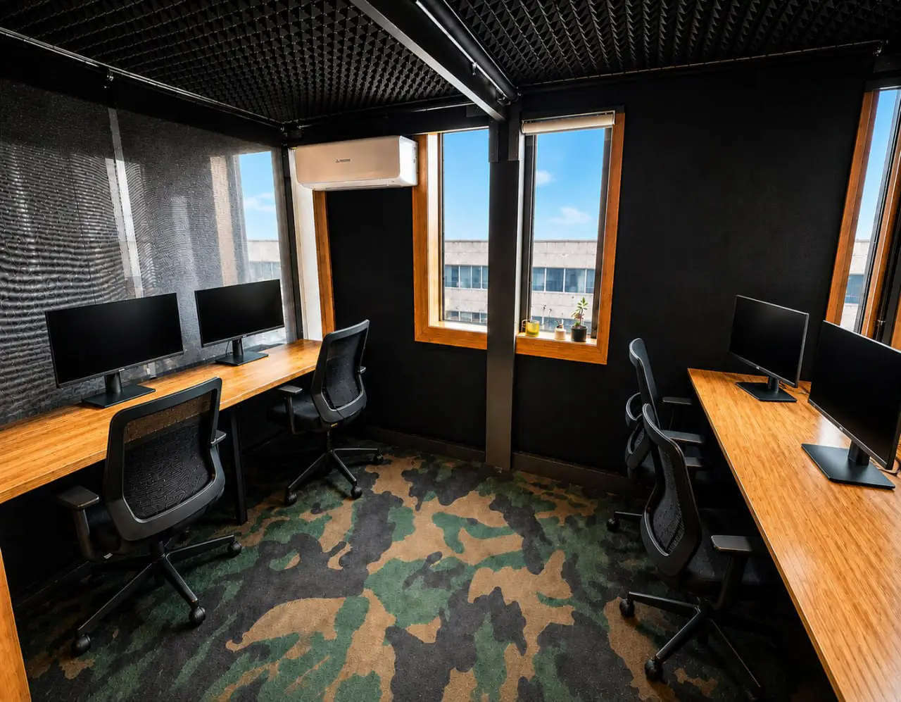 Private office room with computer workstations, wooden desks, black ergonomic chairs, and large windows in a sleek modern coworking space.